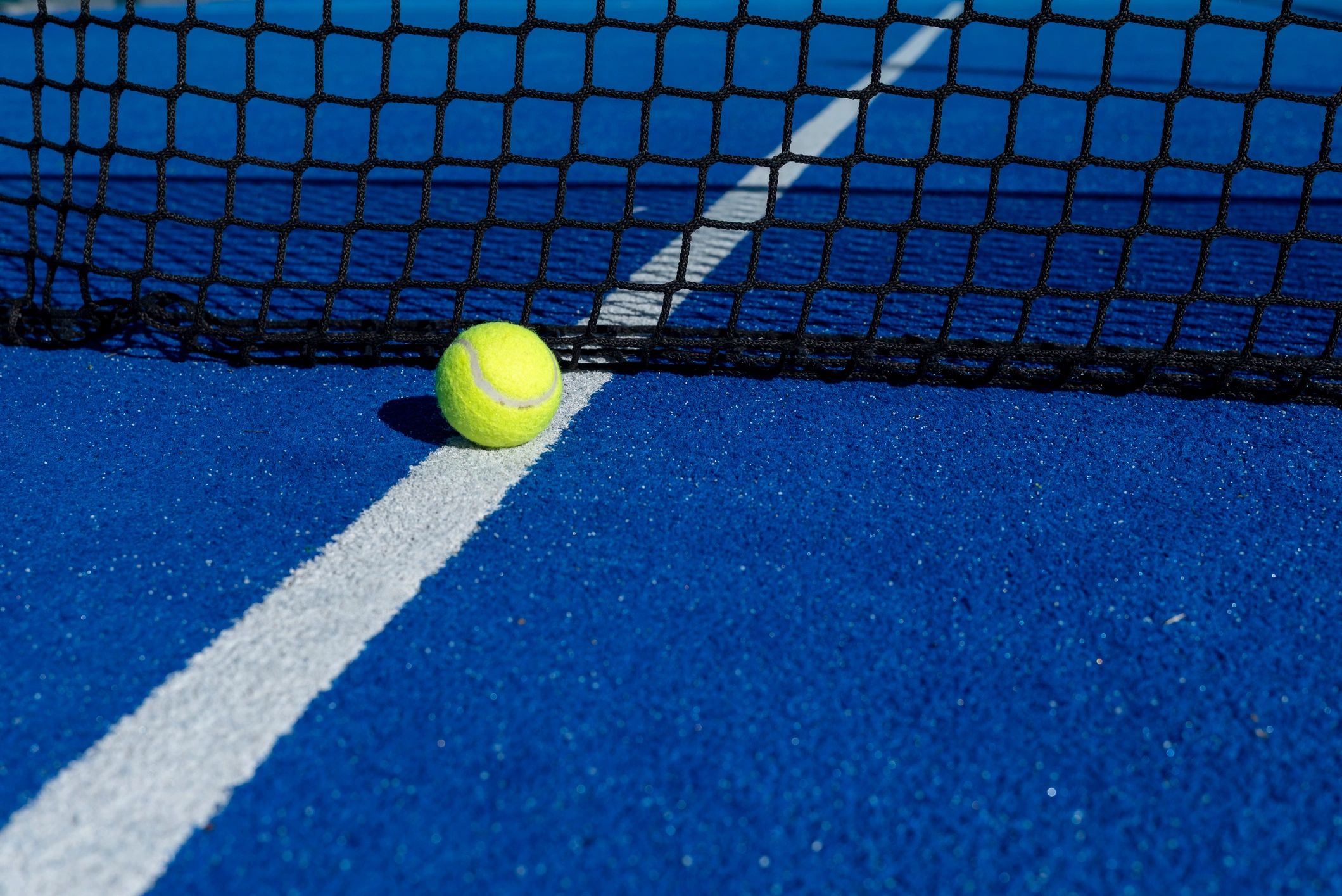 Tennis ball near net on blue court